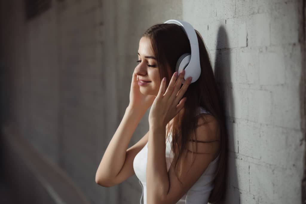 ung kvinde star op ad en mur med tradloese hvide bluetooth hoeretelefoner